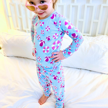 Load image into Gallery viewer, A toddler in a blue and pink two-piece pajama set with a geometric pattern, standing on a bed.