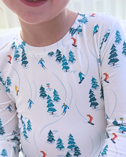 Child wearing a long-sleeve shirt with a winter-themed pattern of skiers and trees.