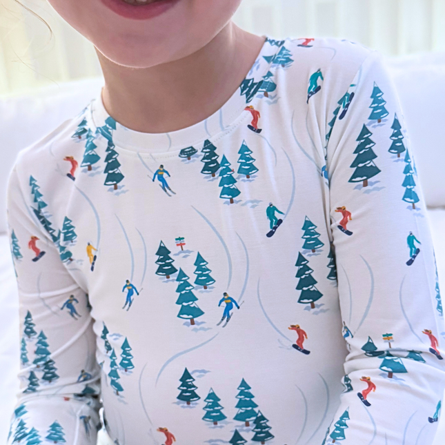 Child wearing a long-sleeve shirt with a winter-themed pattern of skiers and trees.