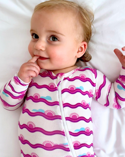 Baby wearing a colorful onesie with a pattern of wavy lines and suns on a white background.