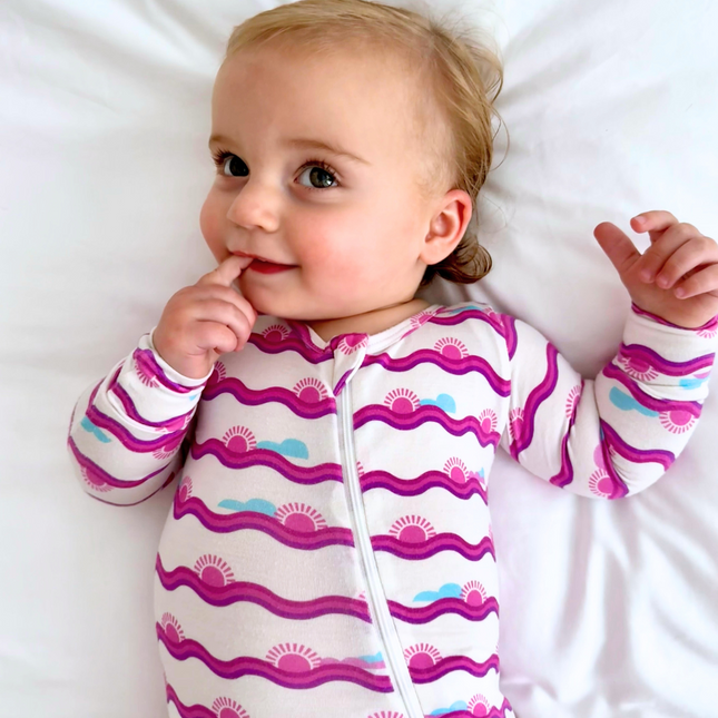 Baby wearing a colorful onesie with a pattern of wavy lines and suns on a white background.