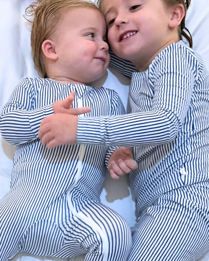 Two toddlers wearing matching navy and white striped pajamas, sitting close and smiling.