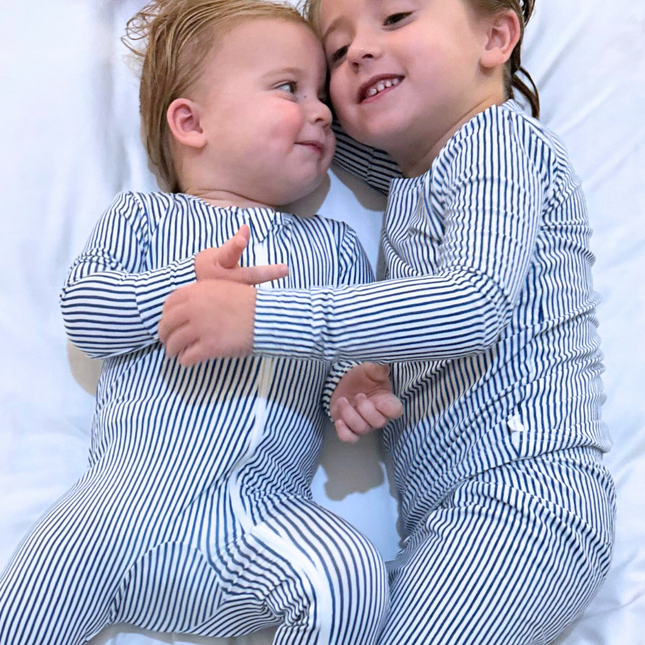 Two toddlers wearing matching navy and white striped pajamas, sitting close and smiling.