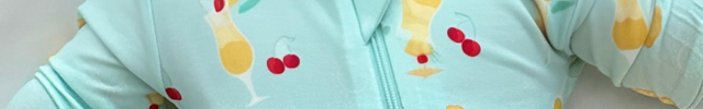 A baby wearing a light blue zippered romper with a fruity print, lying on a white surface.