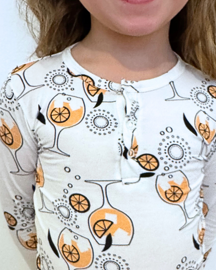 Child wearing a long-sleeve shirt with a wine glass and orange pattern on a plain background