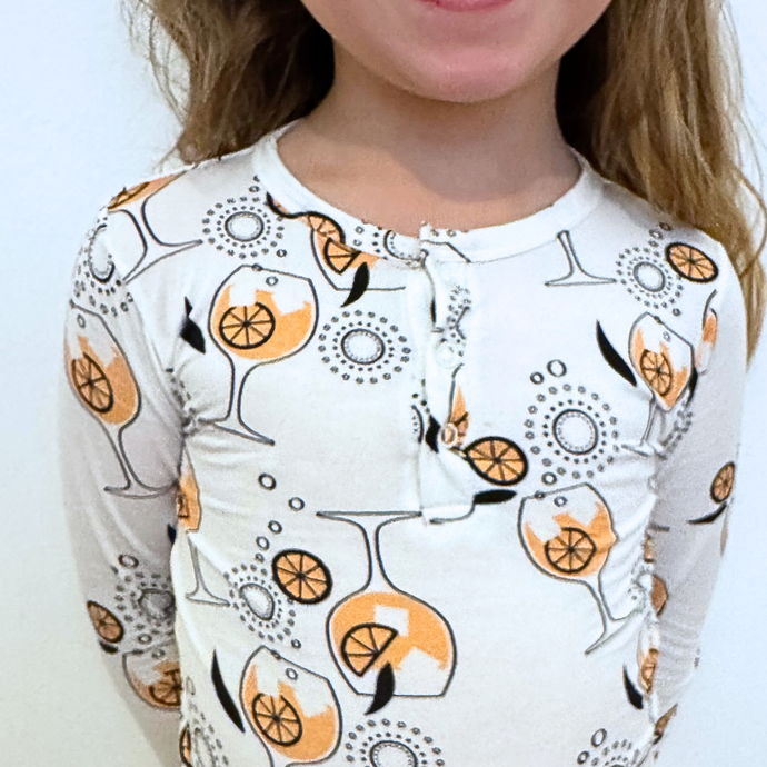 Child wearing a long-sleeve shirt with a wine glass and orange pattern on a plain background
