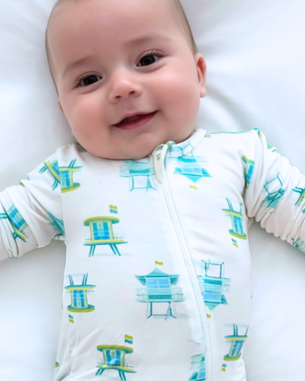 Baby wearing a white onesie with blue and green beach chair pattern on a white background