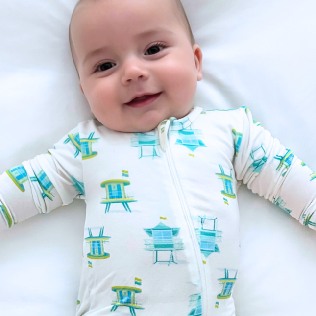 Baby wearing a white onesie with blue and green beach chair pattern on a white background