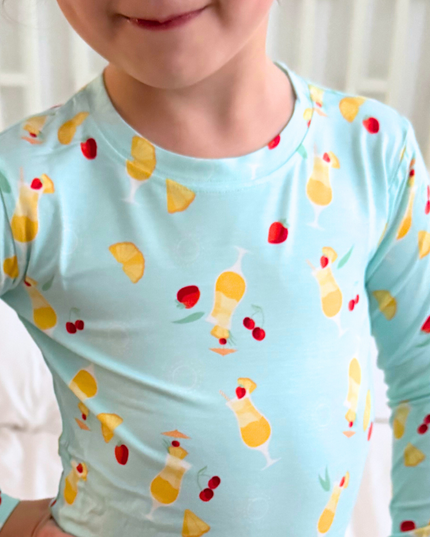 Child wearing a light blue long-sleeve shirt with colorful drink and cherry pattern.