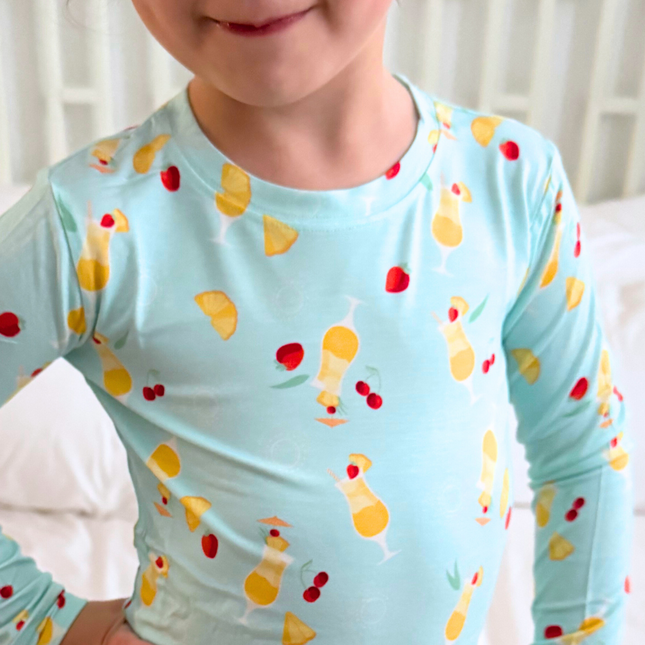 Child wearing a light blue long-sleeve shirt with colorful drink and cherry pattern.