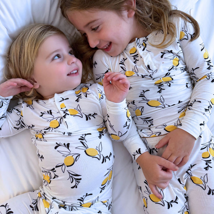 Two children in matching pajamas with lemon pattern on a white background