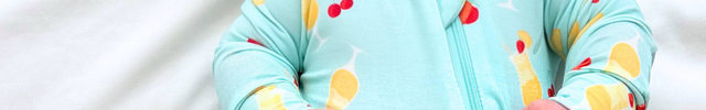 Baby in a colorful onesie with a yellow bow, lying on a white blanket next to a book.