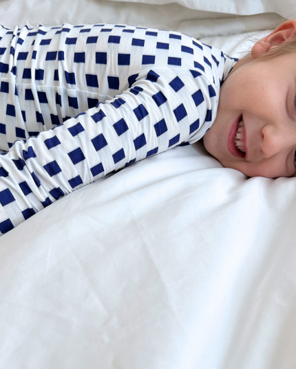 Child wearing blue and white checkered pajamas lying on a white bed.