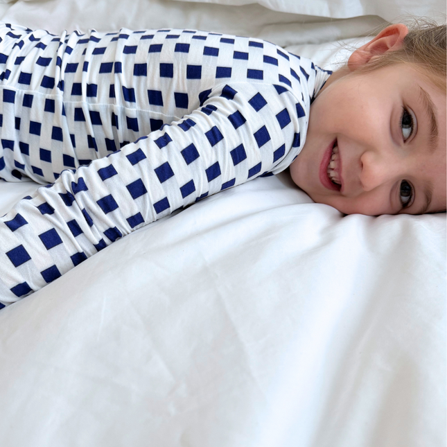 Child wearing blue and white checkered pajamas lying on a white bed.