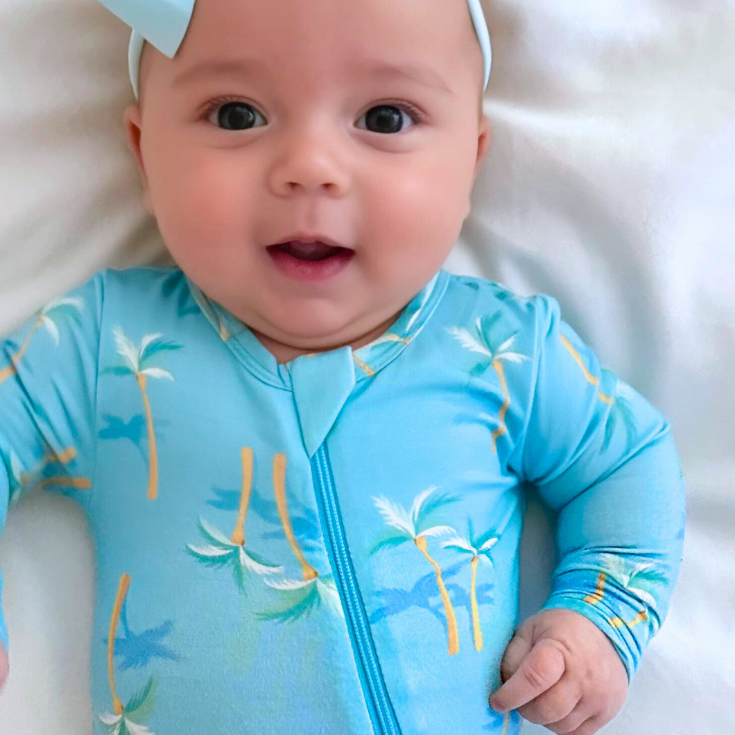 Baby wearing a blue onesie with palm tree design on a white background
