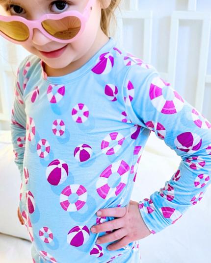 Child wearing a blue long-sleeve shirt with pink and white patterns, sitting on a white couch.