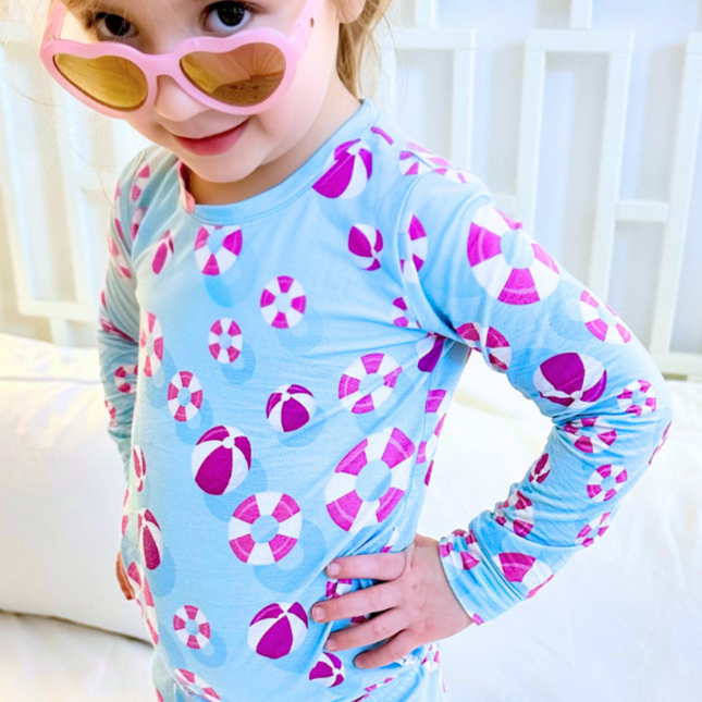 Child wearing a blue long-sleeve shirt with pink and white patterns, sitting on a white couch.