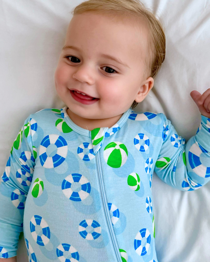 A baby wearing a long-sleeved blue and green zippered romper with a geometric pattern, lying on a white surface.