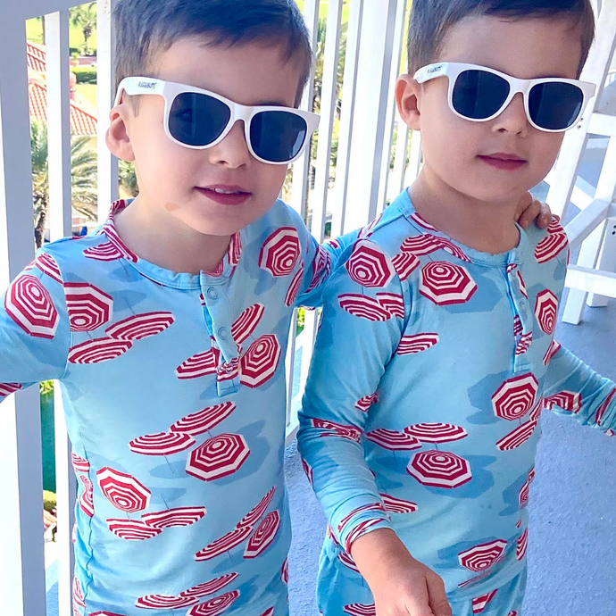 Two children wearing matching blue swimsuits with red umbrella pattern and sunglasses outdoors.