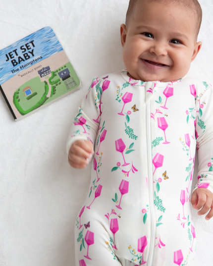 Baby in a floral onesie with a book titled 'Jet Set Baby' on a white background