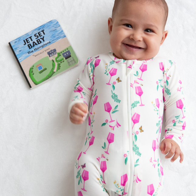 Baby in a floral onesie with a book titled 'Jet Set Baby' on a white background