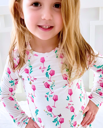 Child wearing a white long-sleeve shirt with pink wine glass pattern against a white background