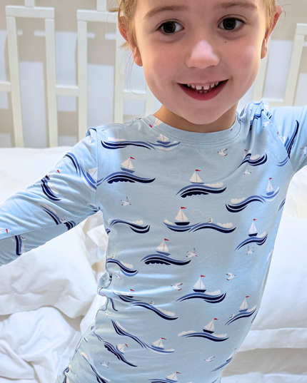 Child wearing a light blue pajama top with boat pattern on a bed.