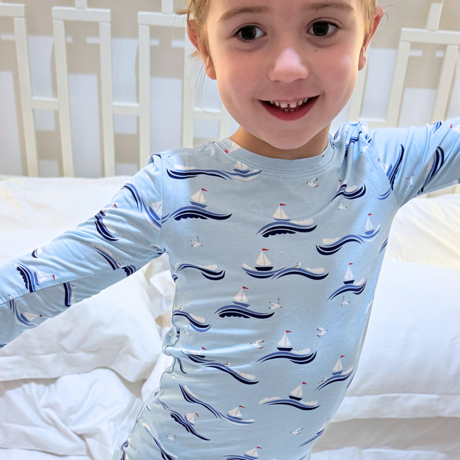 Child wearing a light blue pajama top with boat pattern on a bed.